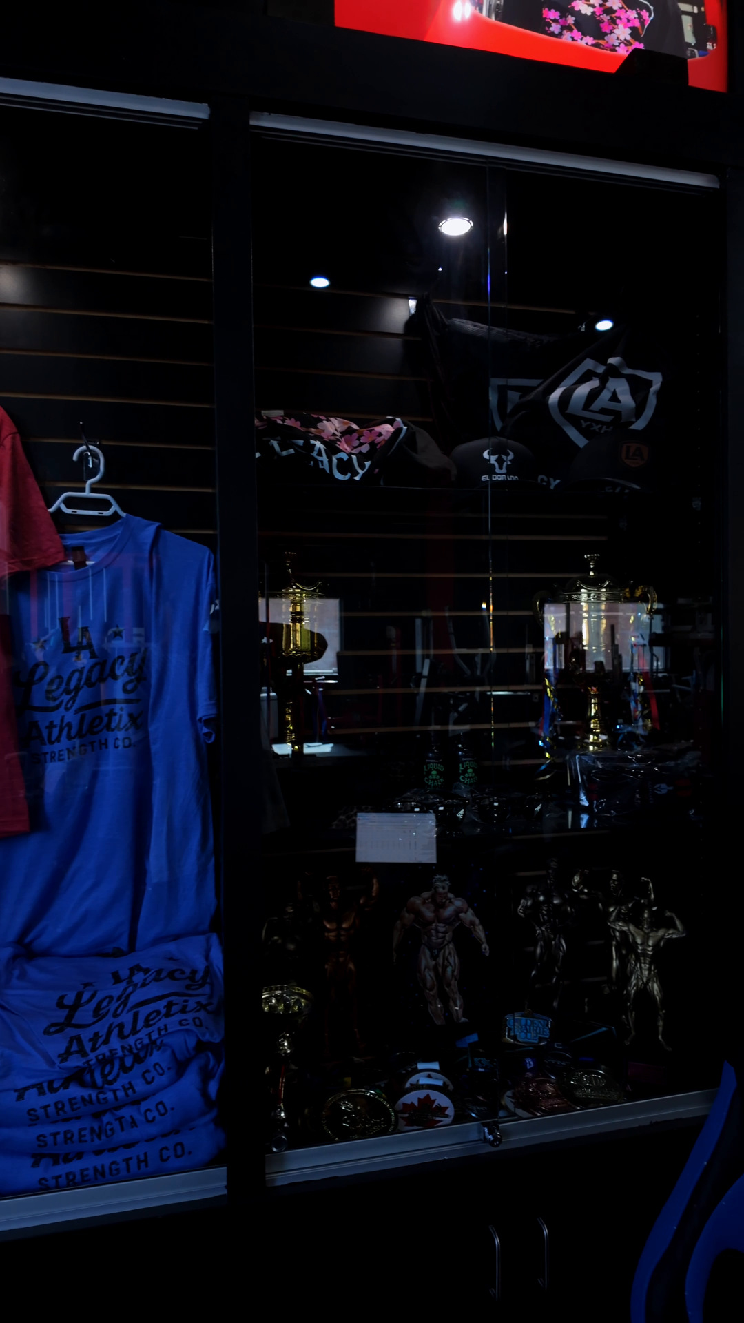 Legacy Athletix branded apparel and bodybuilding trophies in the front display case